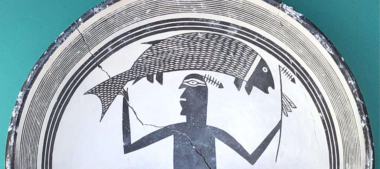 关闭-up of a Native American art replica Mimbres bowl featuring a geometric figure holding a fish aloft.