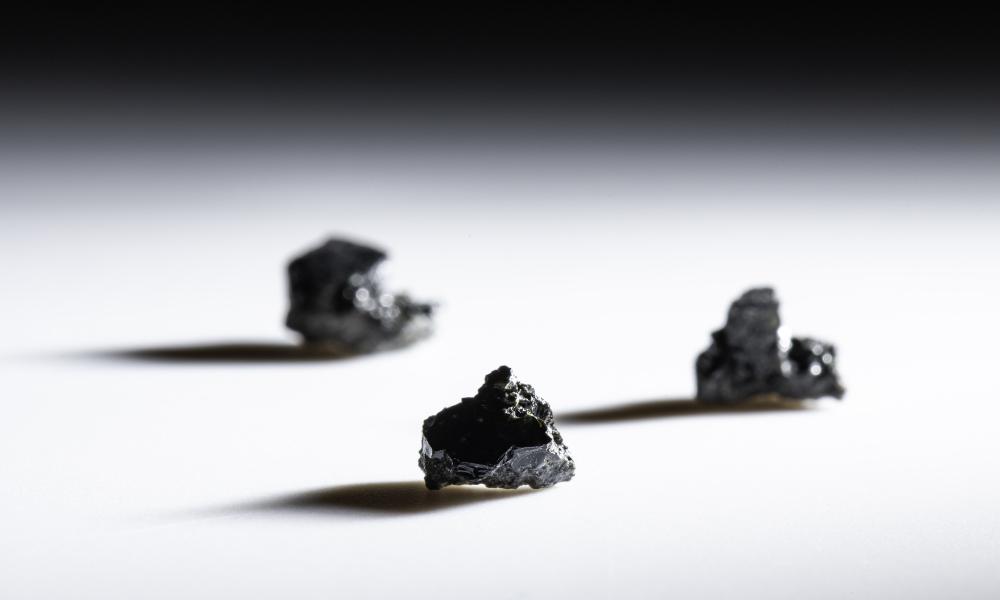 Three samples of lunar glass cast shadows on a white surface and dark background.