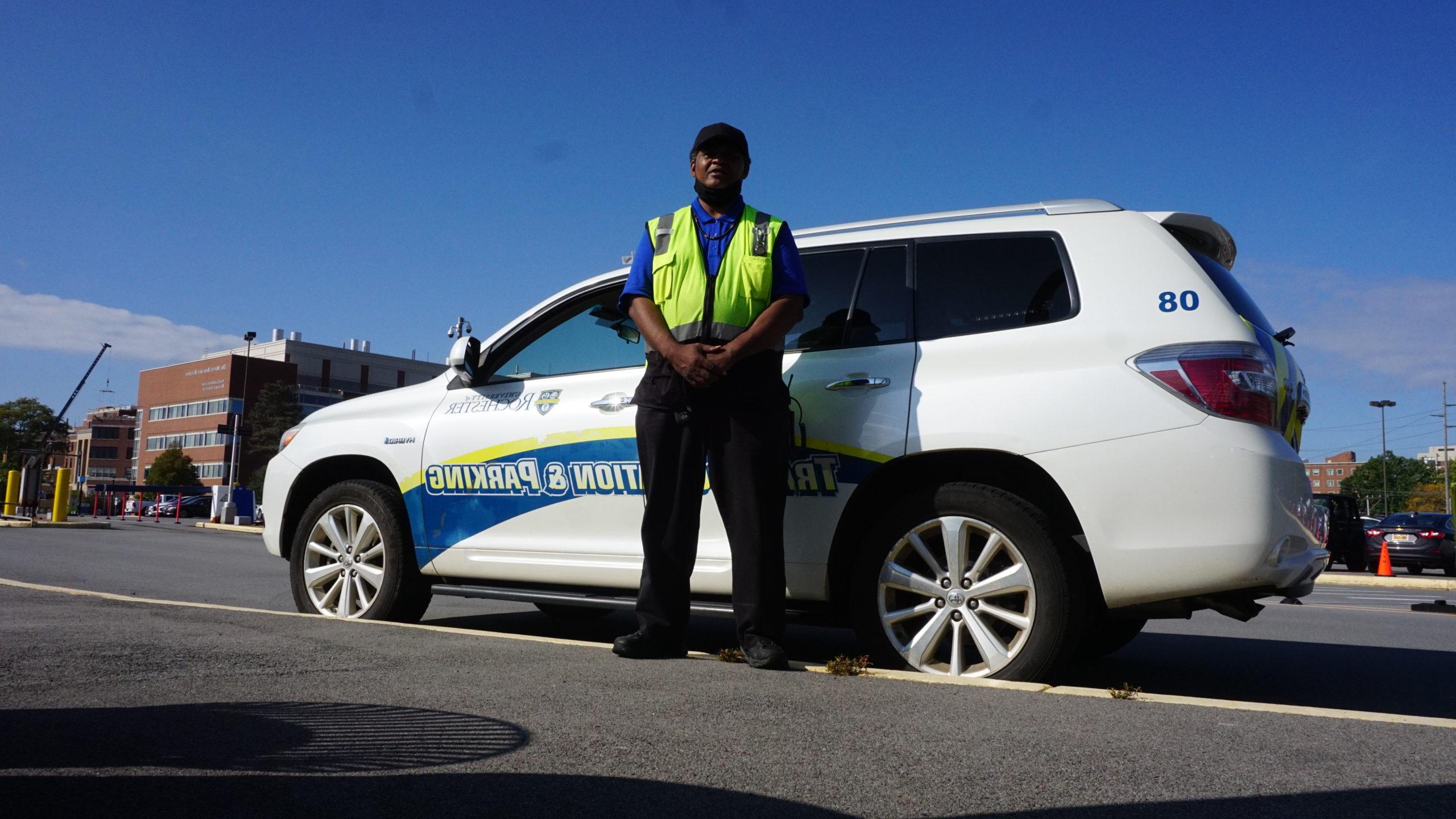 Parking employee standing in front of white Transportation and Parking SUV parked in lot